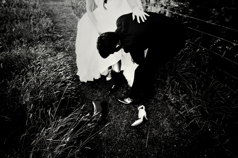 Black and white photograph of a bride putting wellies on