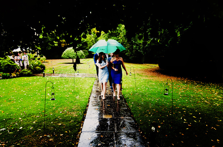 Wedding guestd in the rain with umbrellas outside hengrave hall church.