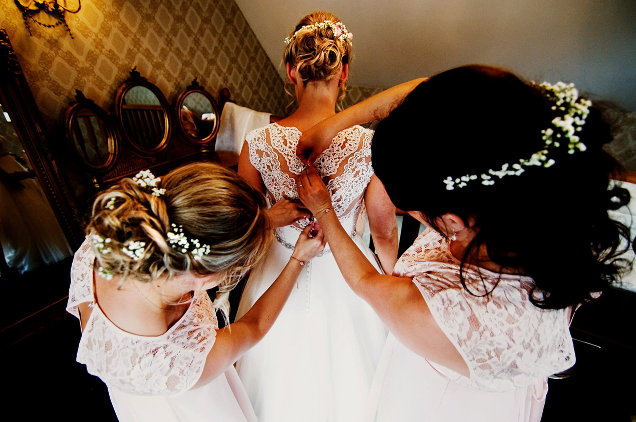 A wedding preview of a bride at Bassmead Manor barns being helped into her wedding dress by her bridesmaids.