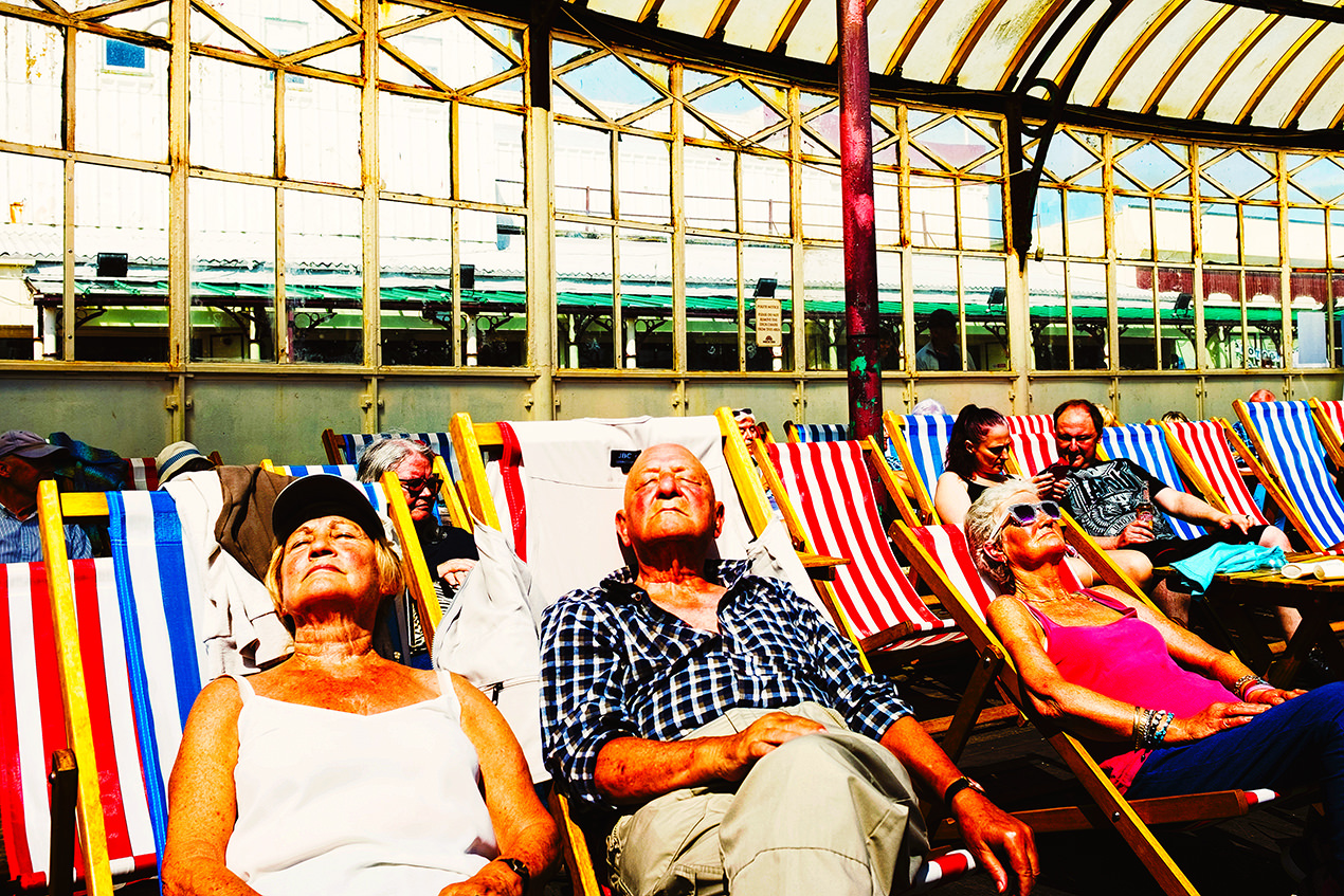Street photography on blackpool's north pier with red and blue deckchairs and people sunbathing.