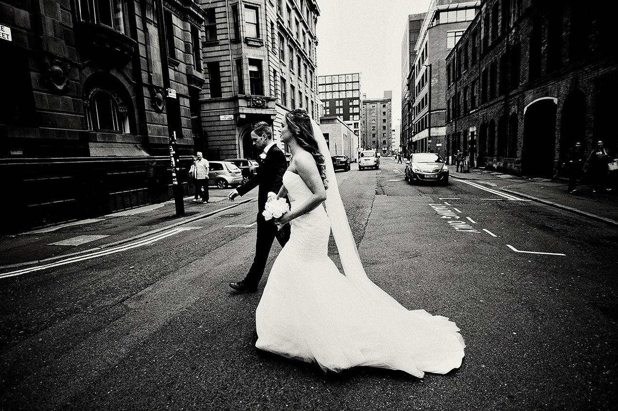 bride and groom walking acrosee a Manchester city street on their wedding day.